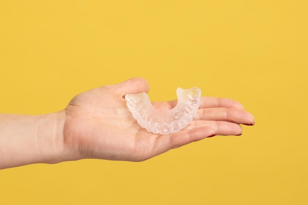 Photo gros plan profil vue latérale portrait d'une main de femme tenant sur le support d'aligneur dentaire de la paume à la clinique dentaire pour un cours de traitement de belles dents prise de vue en studio intérieure isolée sur fond jaune