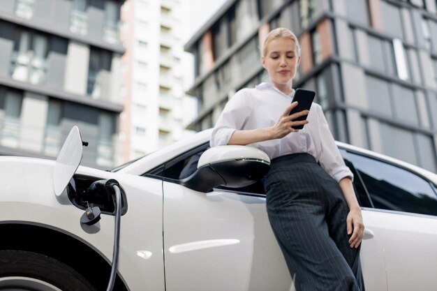 Gros plan progressiste femme parlant au téléphone s'appuyant sur un véhicule électrique