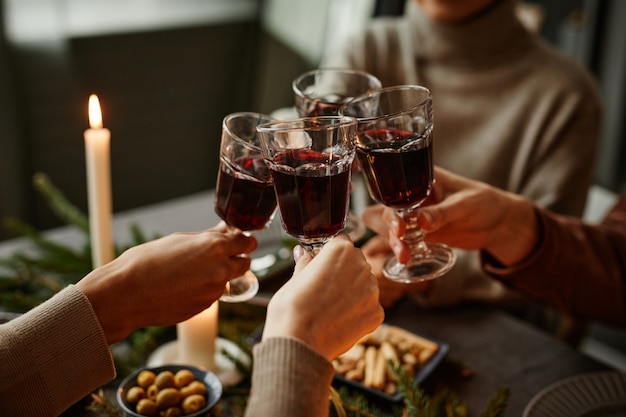 Gros plan sur quatre personnes appréciant le dîner de Noël ensemble et portant un toast avec des verres à vin tout en étant assis...