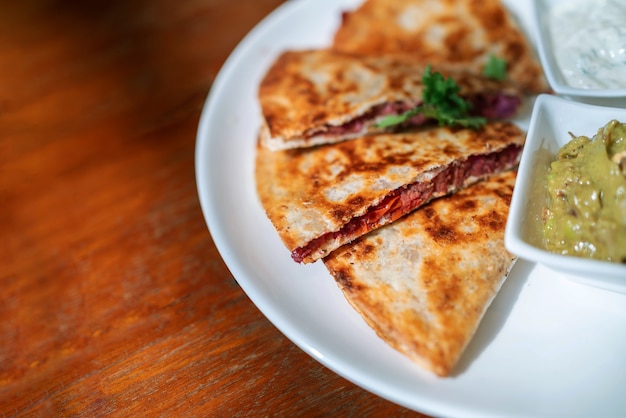 Gros plan de la Quesadilla végétalienne: tortilla de blé entier grillée remplie de patate douce et de haricots rouges servie avec guacamole et sauce Tzaziki.