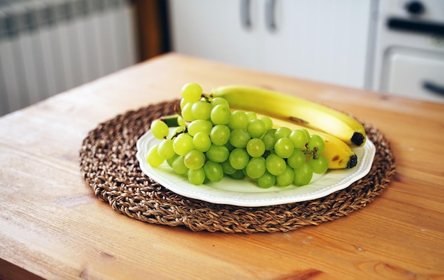 Gros plan de raisins verts et de bananes dans une assiette sur une table de cuisine