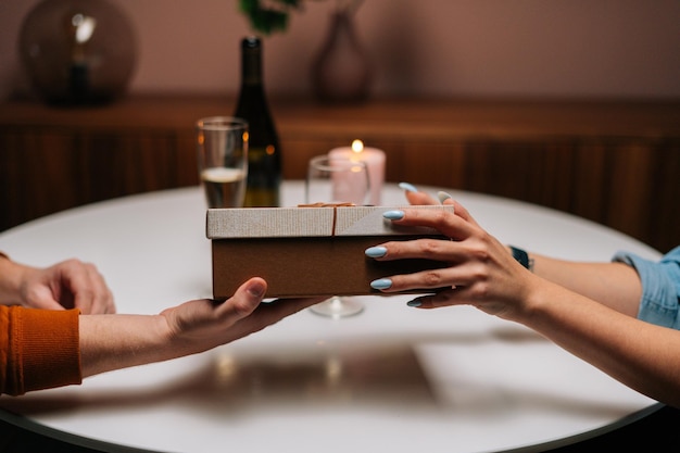 Gros plan recadré d'une femme donnant une boîte emballée avec un cadeau à un homme assis à table avec des bougies le jour de l'anniversaire ou de la Saint-Valentin. Heureux mari recevant un cadeau de sa femme profitant d'un dîner romantique.
