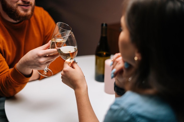 Gros plan recadré d'un jeune couple méconnaissable clinquant des verres de vin à table avec des bougies dans une pièce sombre L