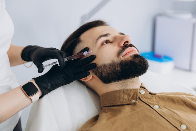 Gros plan de remplissage des lèvres Homme séduisant ayant une injection de beauté au fond du salon de spa masculin