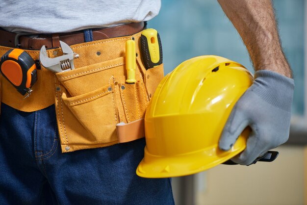 Photo gros plan sur un réparateur portant une ceinture à outils avec divers outils tenant un casque à la main