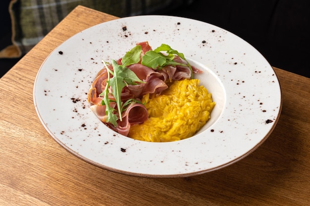 Gros plan de risotto à la citrouille servi avec du jambon prosciutto dans une assiette sélective focus