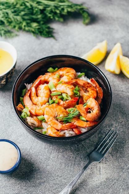 Gros plan de riz aux crevettes frites et aux herbes à côté de la sauce et du citron sur fond gris