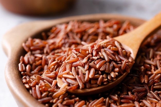 Gros plan de riz rouge cru dans un bol en argile avec une cuillère en bois