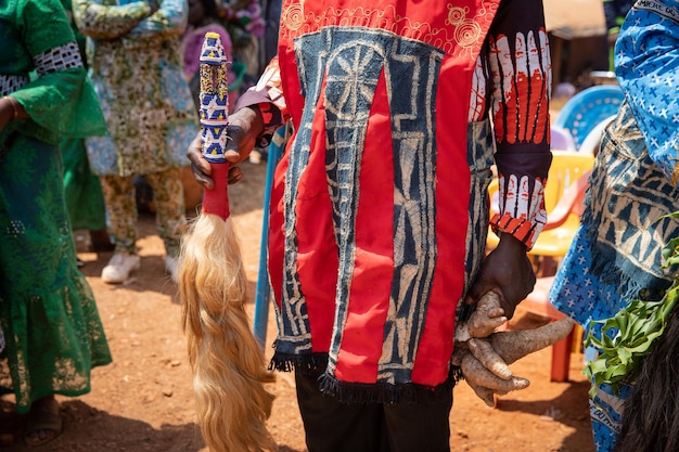 Gros plan d'une robe africaine portée par un homme tenant une queue de cheval décorative traditionnelle et un tubercule lors d'une célébration africaine