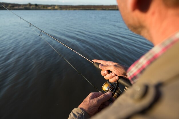 Gros plan de roue de canne à pêche, homme pêchant avec un beau coucher de soleil.