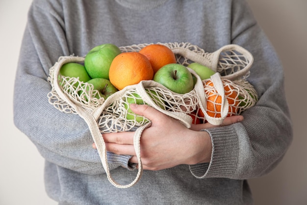 Gros plan sur un sac à cordes avec des fruits frais dans des mains féminines