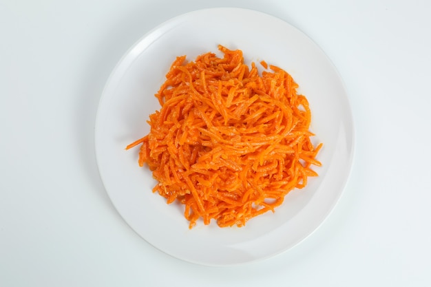 Gros plan de salade de carottes coréenne dans une assiette blanche isolée sur fond blanc. salade coréenne traditionnelle aux carottes