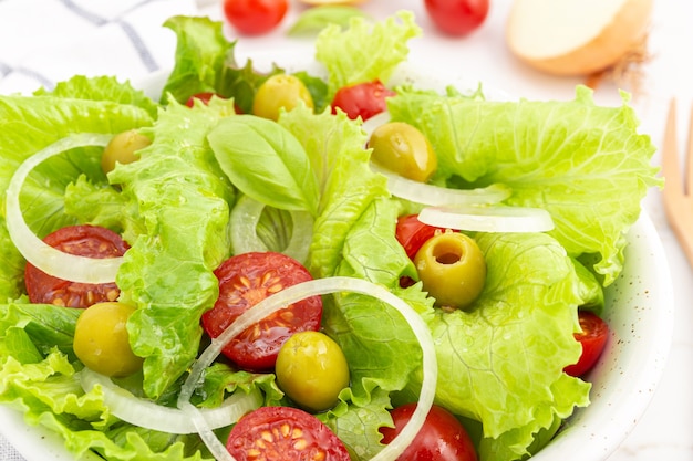 Gros plan d'une salade fraîche et saine avec laitue, oignon, tomate cerise et olives dans un bol. un plat méditerranéen