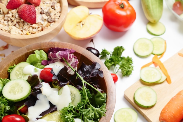 Gros plan de salade de légumes mélangés, muesli et fruits frais sur fond blanc.