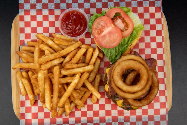 Gros plan de savoureux hamburgers avec de la viande de boeuf ou du fromage et une rondelle d'oignon avec des frites et du ketchup sur un tableau noir sur fond noir