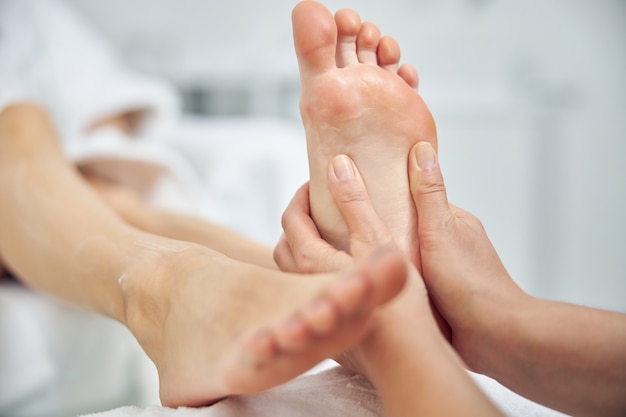 Photo gros plan sur des semelles féminines massées avec les mains d'un professionnel de la beauté dans un centre de cosmétologie