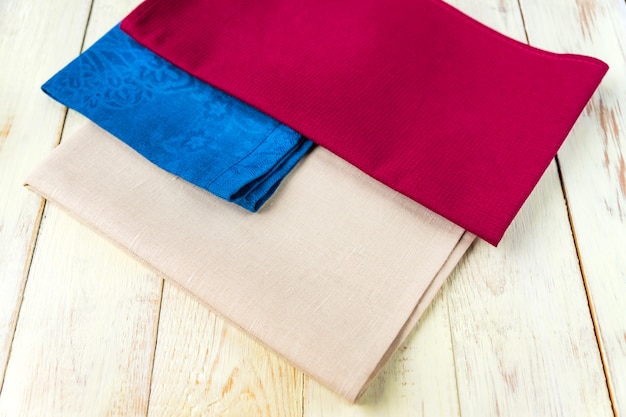 Photo gros plan de serviettes en tissu de couleurs beige, bleu et bordeaux sur table en bois blanc rustique. faible profondeur de champ.