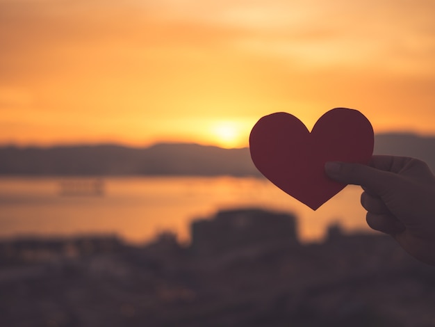 Gros plan et Silhouette de la main tenant un coeur rouge pendant le coucher du soleil