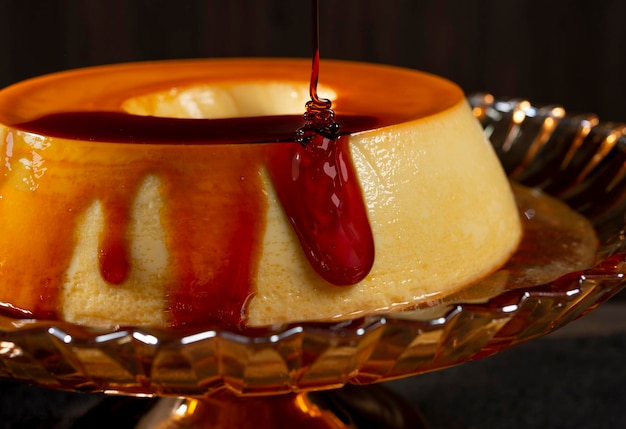 gros plan d'un sirop sucré versé sur du pudding à la crème au caramel sur un support à gâteau en verre