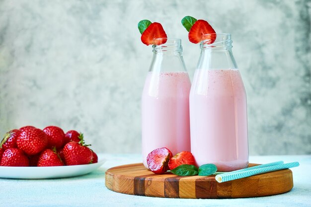 Gros plan sur un smoothie aux fraises ou un milk-shake dans un pot en verre avec des baies sur fond de béton bleu