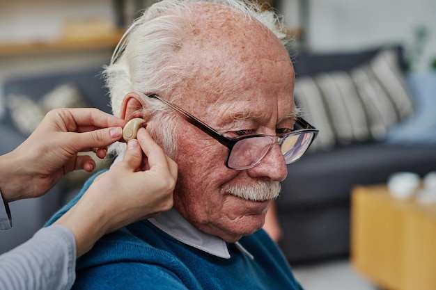 Gros plan d'un soignant portant une prothèse auditive dans l'oreille d'un homme âgé ayant des problèmes d'audition