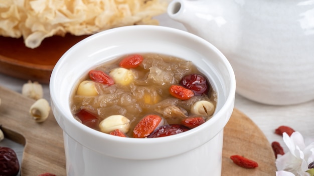 Photo gros plan sur une soupe traditionnelle chinoise de champignons blancs de neige sucrés avec des graines de lotus, des dattes rouges (jujube) et du goji (baie de goji, gojiberry) sur fond blanc.