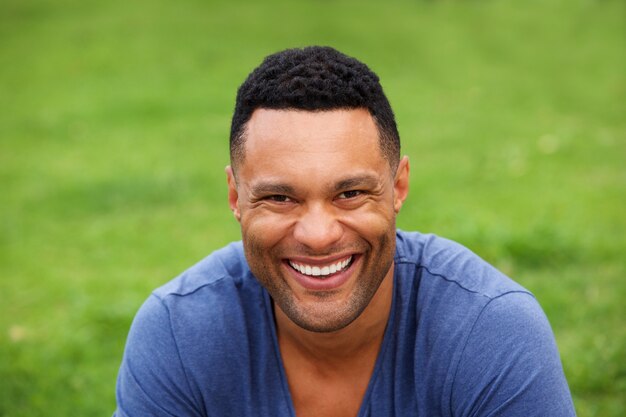 Photo gros plan souriant jeune homme assis à l'extérieur contre l'herbe verte