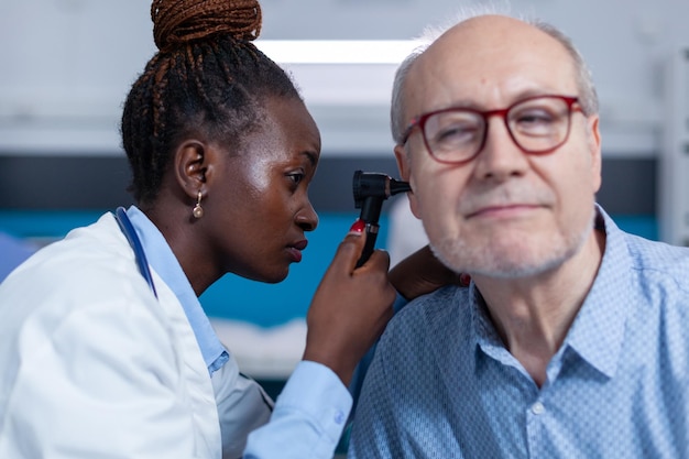 Gros plan sur un spécialiste en otologie examinant une personne âgée malade à l'aide d'un otoscope pour vérifier le mal d'oreille. Spécialiste de la santé examinant l'oreille d'un patient malade à la retraite à l'aide d'un instrument d'otologie.