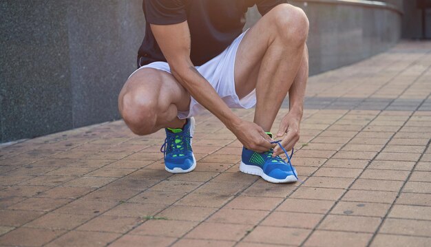 Gros plan d'un sportif attachant des lacets sur ses baskets de course bleues tout en se préparant pour