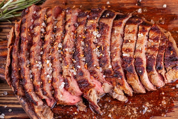 Gros plan de steak de boeuf grillé en tranches avec des épices sur une planche à découper en bois