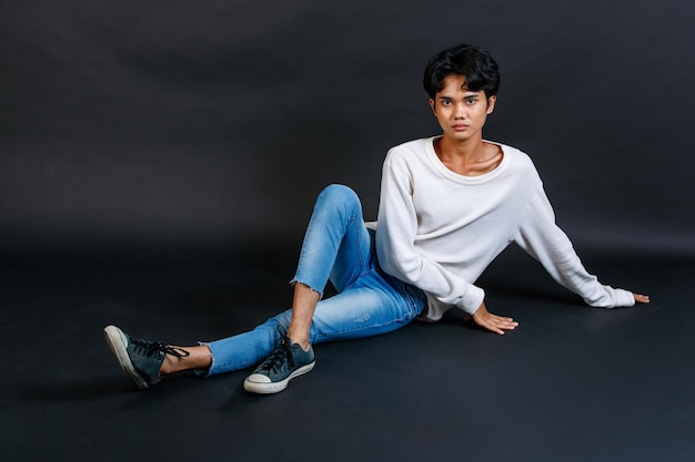 Gros plan studio photo de jeune asiatique LGBTQ gay glamour heureux beau mannequin homosexuel bisexuel masculin en tenue décontractée de chemise à manches longues assis souriant posant gesticulant sur fond noir