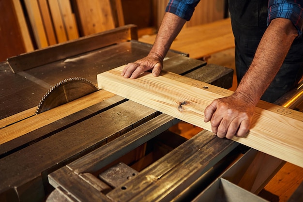 Gros plan d'une table de coupe de bois avec une scie circulaire électrique Charpentier professionnel senior en planche de bois de coupe uniforme à la fabrication de menuiserie de scierie