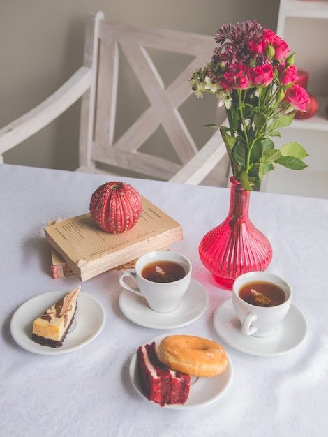 Photo gros plan sur la table: thé, beignet, gâteau, fleurs dans un vase, bougies, livres