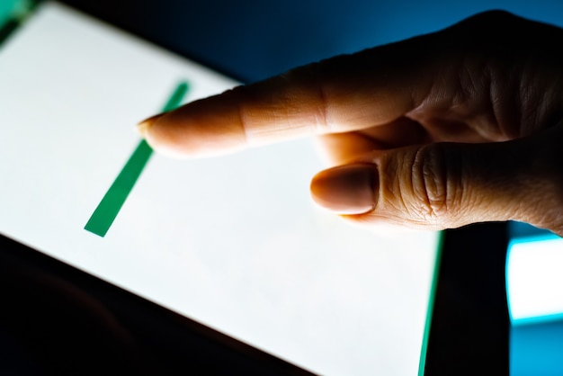 Gros plan de la tablette avec écran blanc et main des utilisateurs sur fond sombre
