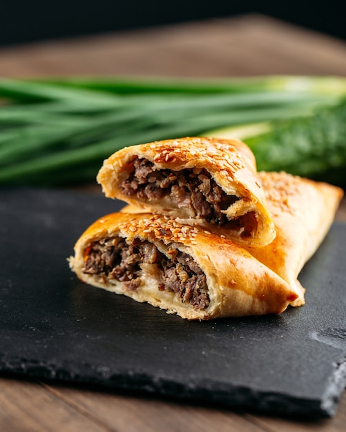 Gros plan sur la tarte au four plat oriental coupé avec de la viande samsa sur la plaque de pierre noire