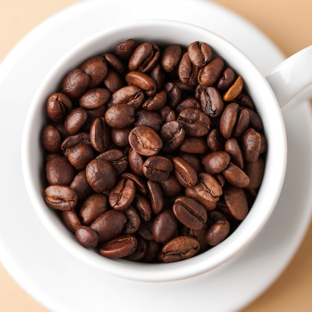 Gros plan d'une tasse blanche avec des grains de café arabica. Photo carrée.