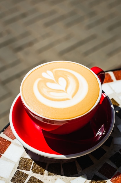 Un gros plan d'une tasse de café cappuccino rouge fraîchement préparé sur une table en pierre de mosaïque d'une terrasse de café sur une journée ensoleillée