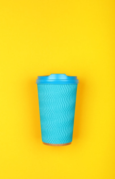 Gros plan d'une tasse de café à emporter papier bleu pastel jetable serti sur fond jaune vif, mise à plat, vue de dessus surélevée, directement au-dessus