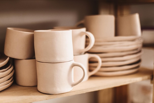 Gros plan sur des tasses et des tasses en argile faites à la main sur des étagères en bois au studio de poterie