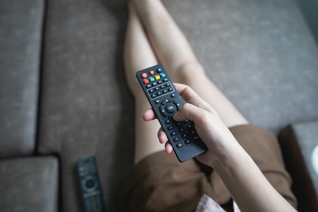 Gros plan Télécommande de télévision chez une jeune femme chemise rose mains pointant vers le téléviseur et l'allumer ou l'éteindre sélectionner une chaîne en regardant la télévision sur un canapé à la maison dans le salon se détendre