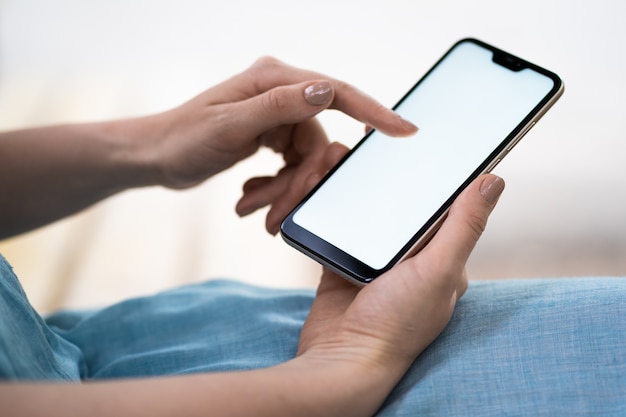 Gros plan d'un téléphone avec un écran blanc dans des mains féminines. Une femme avec une belle manucure tient un téléphone. Technologies modernes, smartphone. Espace de copie.