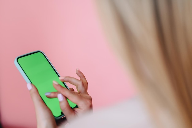 Gros plan d'un téléphone à écran vert et de mains féminines faisant semblant de cliquer sur un fond rose