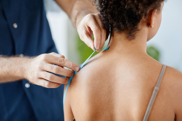 Photo gros plan d'un thérapeute en réadaptation mettant du ruban physio sur l'épaule d'une jeune femme pour soulager les muscles p