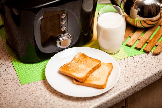 Gros plan de toasts cuits au four allongé sur un plat blanc avec un verre de lait