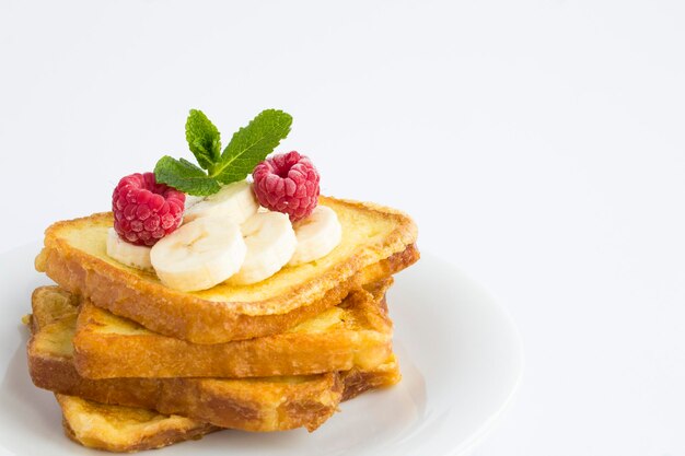 Gros plan sur des toasts français avec banane et framboise sur la plaque blanche sur fond blanc. Copiez l'espace.