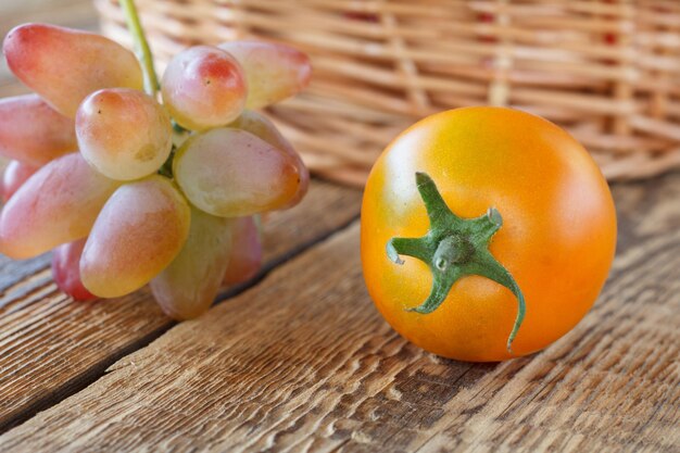 Gros plan tomate jaune, raisin et panier en osier sur fond en bois. Faible profondeur de champ.