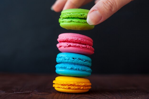 Gros plan de tour de macarons colorés sur fond noir. La main féminine prend un cookie