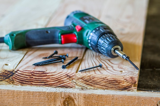 Gros plan d'un tournevis électrique avec des vis portant sur une vieille table en bois brut ou des planches naturelles vintage. Concept de construction, de réparation et d'entretien domestique