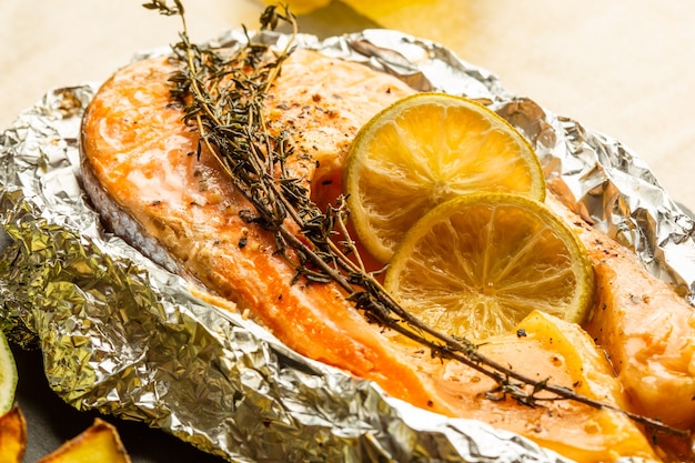 Gros plan d'une tranche de poisson cuite dans du papier d'aluminium avec une branche de thym et des tranches de citron sur le dessus