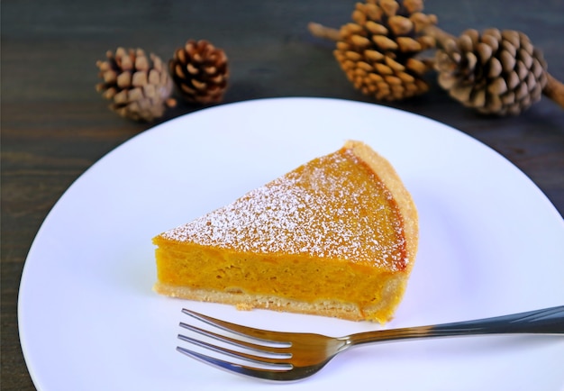 Gros plan d'une tranche de tarte à la citrouille alléchante et de pommes de pin sèches en toile de fond